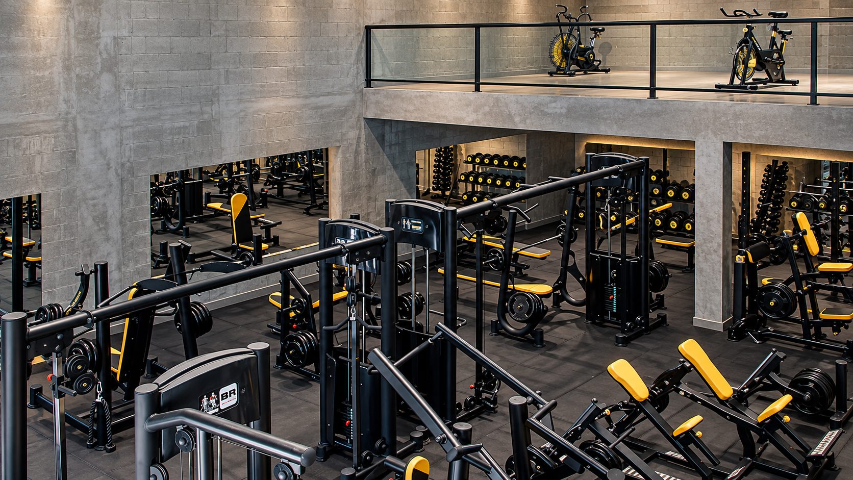 Vista de cima da sala de musculação com aparelhos pretos e amarelos